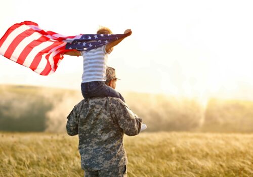 A man in uniform with a little boy on his shoulders holding an American flag